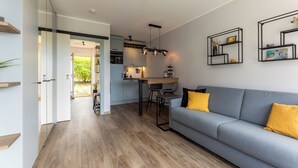 A modern living room with a grey sofa, wooden flooring, and a kitchen in the background. - Isola - Wenningstedt-Braderup (Sylt) (Wenningstedt-Braderup (Sylt))