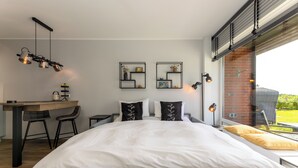A modern bedroom with a bed, a desk, and chairs. There are wall-mounted shelves with decorative items. - Isola - Wenningstedt-Braderup (Sylt) (Wenningstedt-Braderup (Sylt))