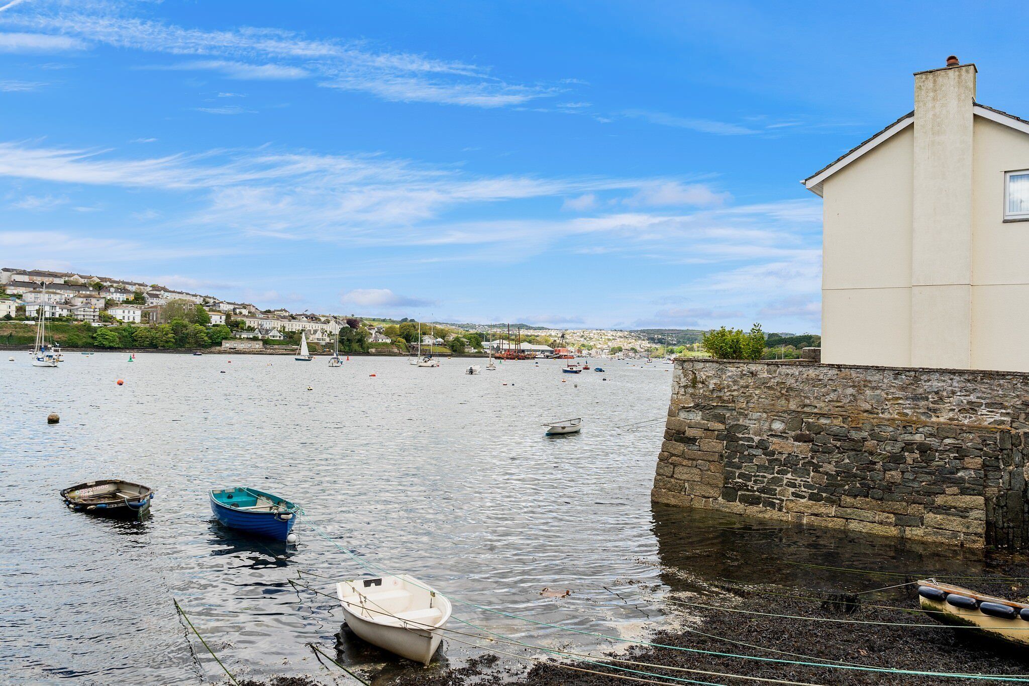 A harbor with boats, a stone wall, and a building with a chimney.