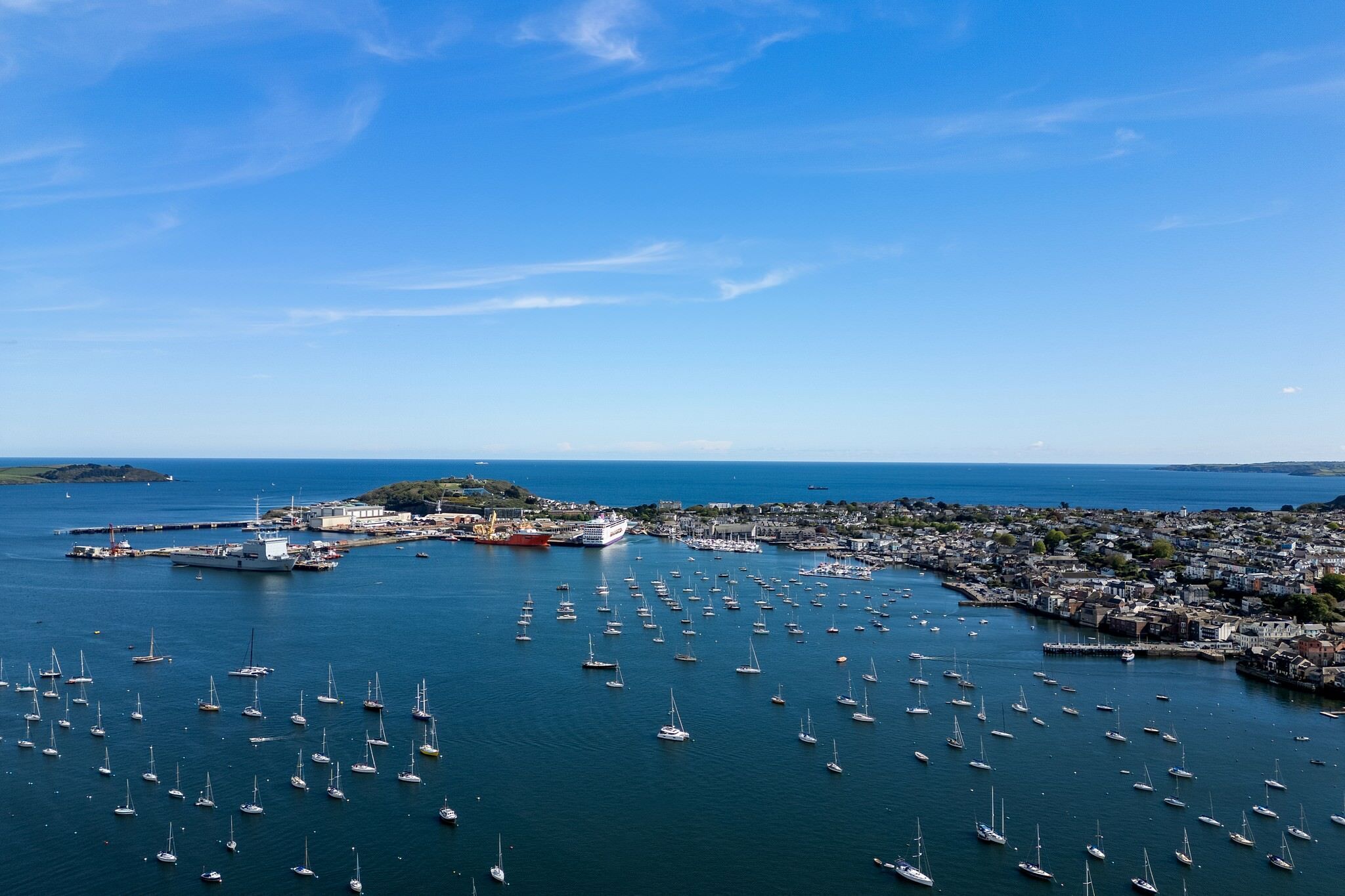 Vue aérienne d’une ville côtière, avec de nombreux bateaux amarrés dans le port et un grand navire de croisière en arrière-plan.