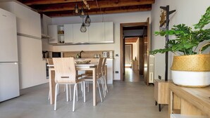 A modern kitchen with white cabinets, a wooden dining table, and chairs. There is a large woven basket on a wooden sideboard. - Ca' Linda By Case al Lago (Desenzano del Garda)