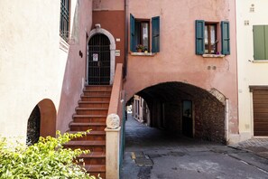 A narrow alleyway with a stone staircase leading to a door, flanked by buildings with arched windows and a brick archway.