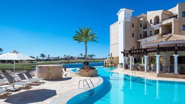 Ein Swimmingpool mit Liegestühlen und einer Palme, umgeben von einem Gebäude mit Balkonen.