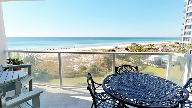 Ein Balkon mit Tisch und Stühlen mit Blick auf Strand und Meer.