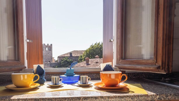A table with various cups and saucers by an open window overlooking a historic building.