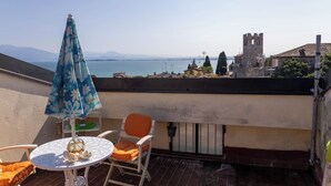 A terrace with a table and chairs, a blue umbrella, and a view of a historic tower and water.