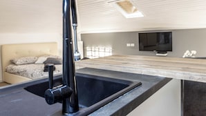 A modern kitchen with a black sink, a built-in oven, and a flat-screen TV mounted on the wall.