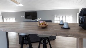 A modern kitchen with a wooden countertop, two bar stools, a television, and a coffee machine.