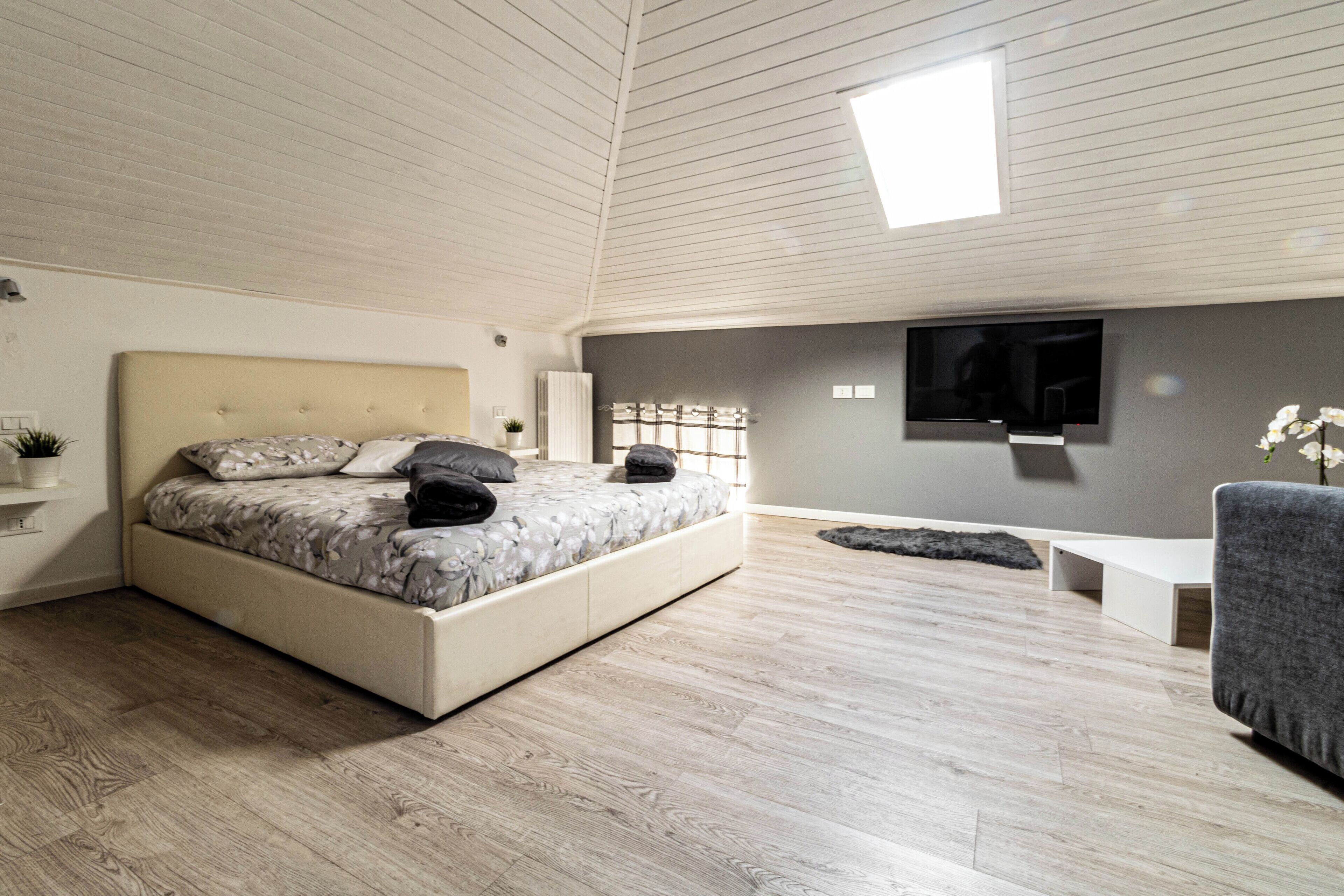 Un dormitorio con cama, televisor, banco y ventana.
