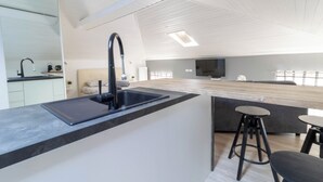 A modern kitchen with a black faucet, a built-in sink, and a wooden countertop. There are two stools and a flat-screen TV mounted on the wall.