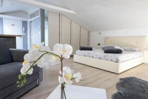 Un dormitorio moderno con cama, sofá y un jarrón de orquídeas blancas.