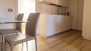 A modern kitchen with white cabinets, a glass dining table, and two chairs. - Maison 140 By Case al Lago (Lonato)