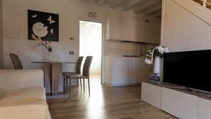 A modern living room with a sofa, dining table, chairs, and a TV on a cabinet. - Maison 140 By Case al Lago (Lonato)