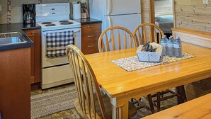A wooden-paneled kitchen with a stove, microwave, refrigerator, and dining table with chairs. - Ahmic Lake Resort's Black Bear Cottage (Magnetawan)