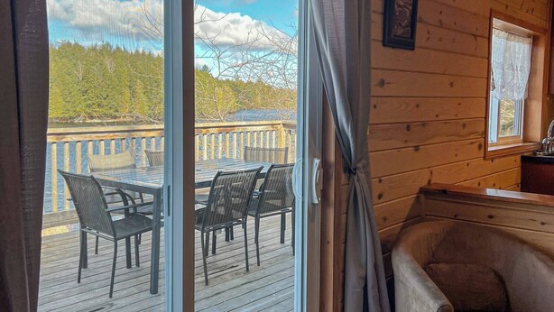 A wooden cabin interior with a sliding glass door leading to an outdoor deck with chairs and a table. - Ahmic Lake Resort's Black Bear Cottage (Magnetawan)