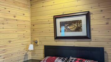 A wooden-paneled room with a bed, a ceiling fan, a framed picture on the wall, and a bedside lamp.