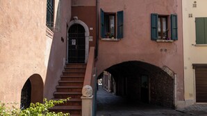 Una calle estrecha con una escalera de piedra que lleva a la entrada de un edificio, una ventana pequeña con contraventanas y un arco de piedra.