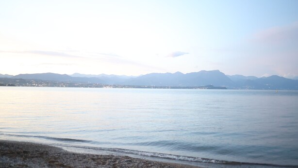 Un lago tranquilo con una cadena montañosa distante y el horizonte de una ciudad.