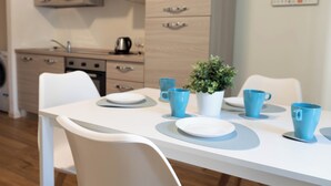Una cocina moderna con armarios de madera, un fregadero y una estufa. Hay una mesa de comedor con tazas azules y una planta en maceta.