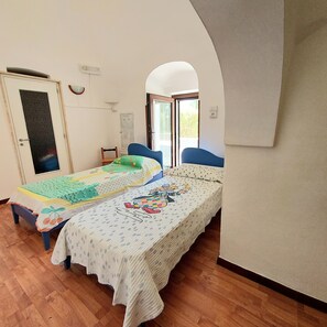 Cozy retreat with a large bed, wooden chair, and desk, offering a peaceful view of the surrounding greenery.