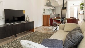 Una sala de estar moderna con un televisor de pantalla plana, muebles de madera oscura, un sofá beige y un comedor con una mesa y sillas de vidrio.