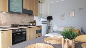 A modern kitchen with wooden cabinets, a stove, and a sink. There is a bed with a gray bedspread and a potted plant on it.