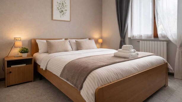 A neatly arranged bedroom with a bed, bedside tables, a lamp, and a window with curtains.