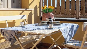 A table with a patterned tablecloth, a vase with yellow flowers, a teapot, and cups on a balcony with a wooden fence in the background. - Casa Monia By Case al Lago (Lonato)
