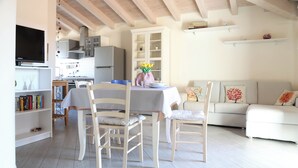 A modern kitchen with white cabinetry, a dining table with chairs, a sofa, and a TV mounted on the wall. - Casa Monia By Case al Lago (Lonato)