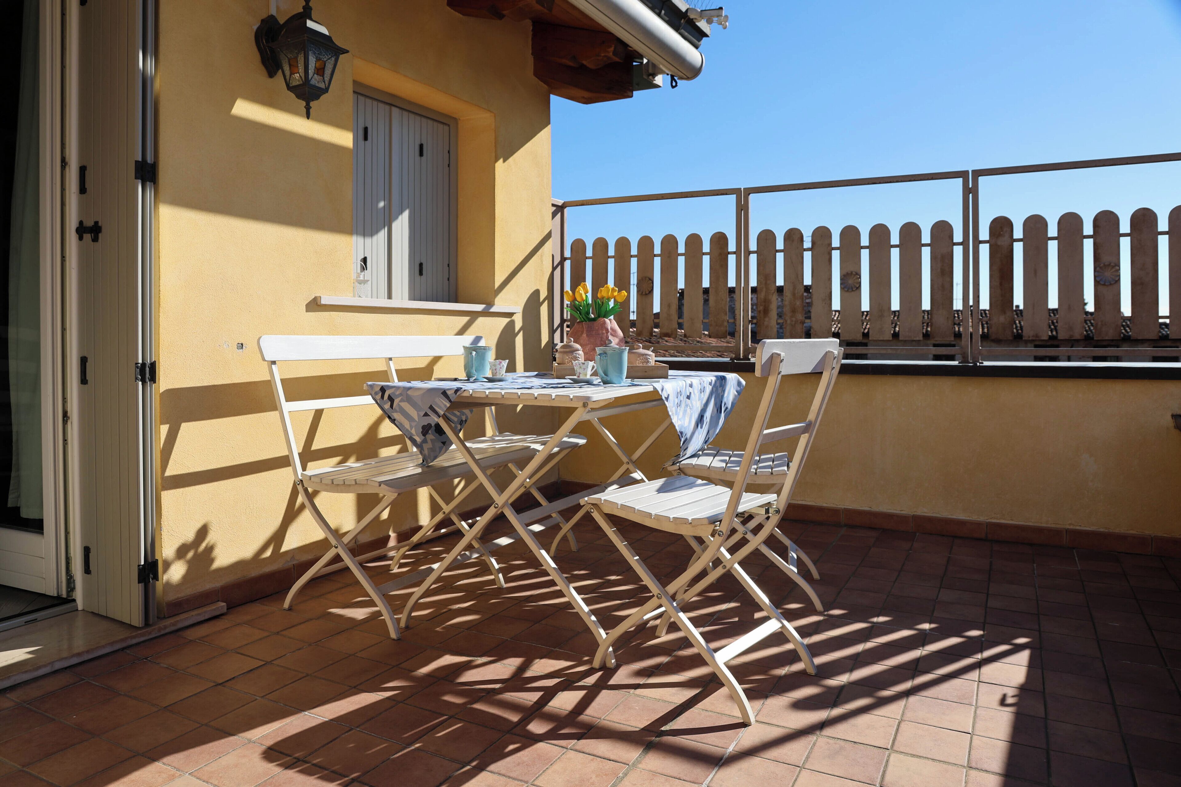 Un balcone con tavolo e sedie, una pianta in vaso e vista su una recinzione di legno.