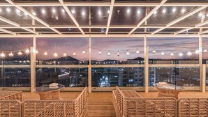 A rooftop terrace with wicker furniture, string lights, and a city view at dusk. - Gridt Hotel (Gyeongju)