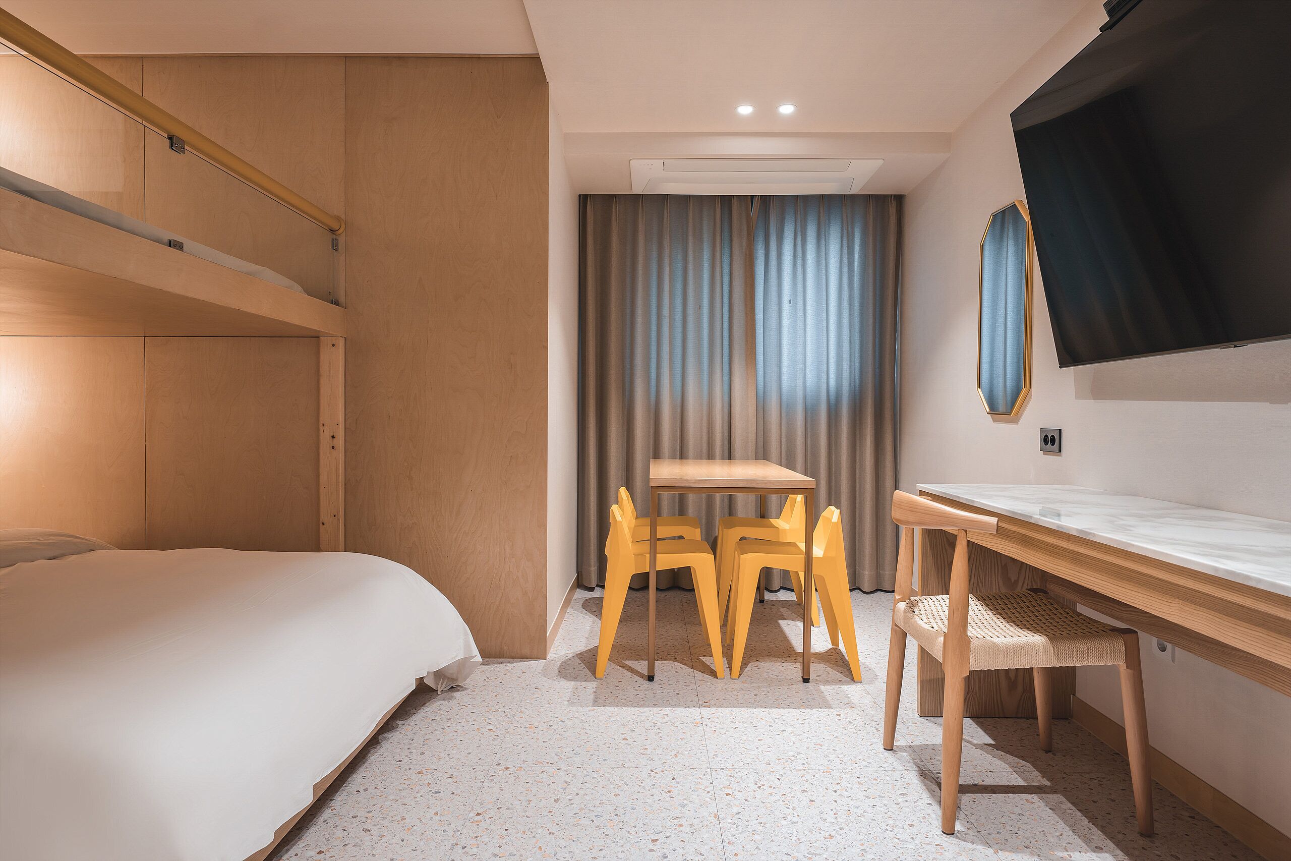 Habitación de hotel con una cama, un escritorio, dos sillas, un televisor y una cortina.