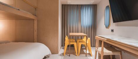 Habitación de hotel con una cama, un escritorio, dos sillas, un televisor y una cortina.