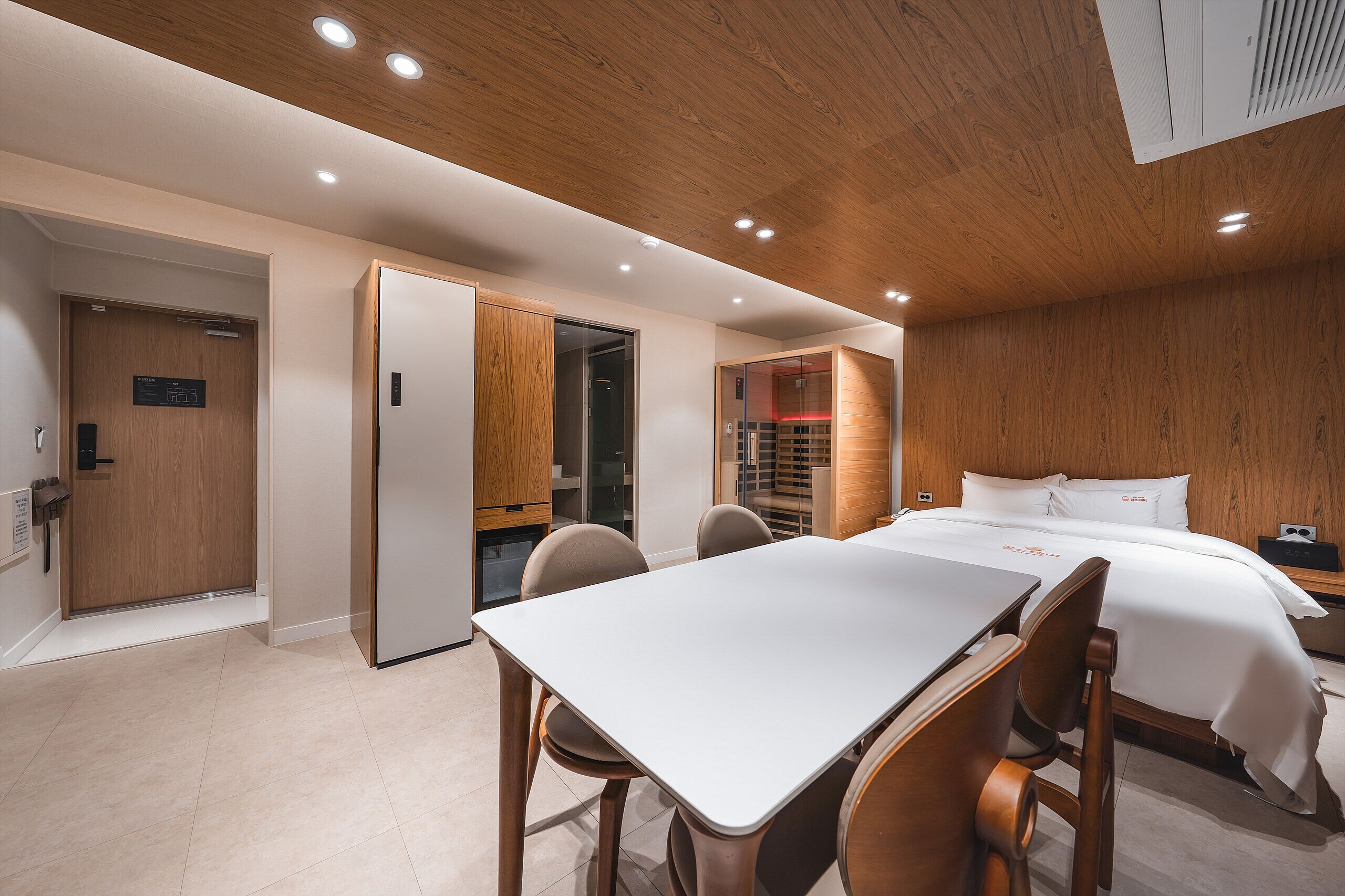 A hotel room with a wooden ceiling, a bed with white bedding, a desk with chairs, and a wardrobe.