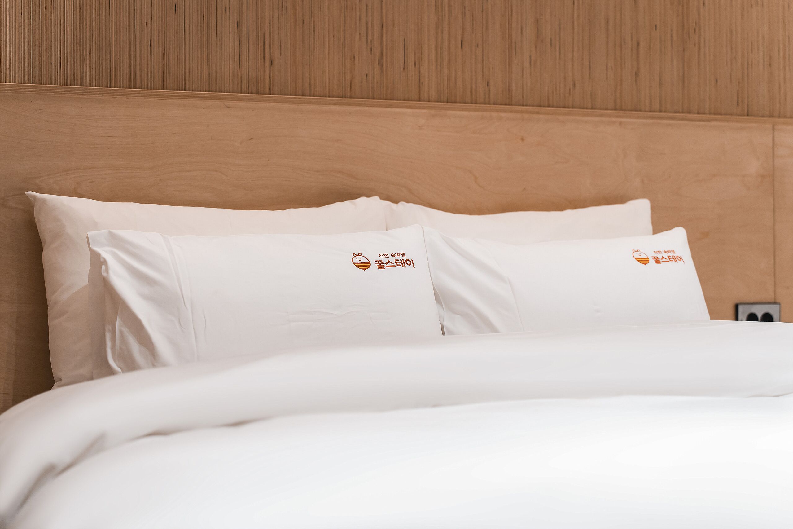 A bed with white bedding and pillows featuring a logo.