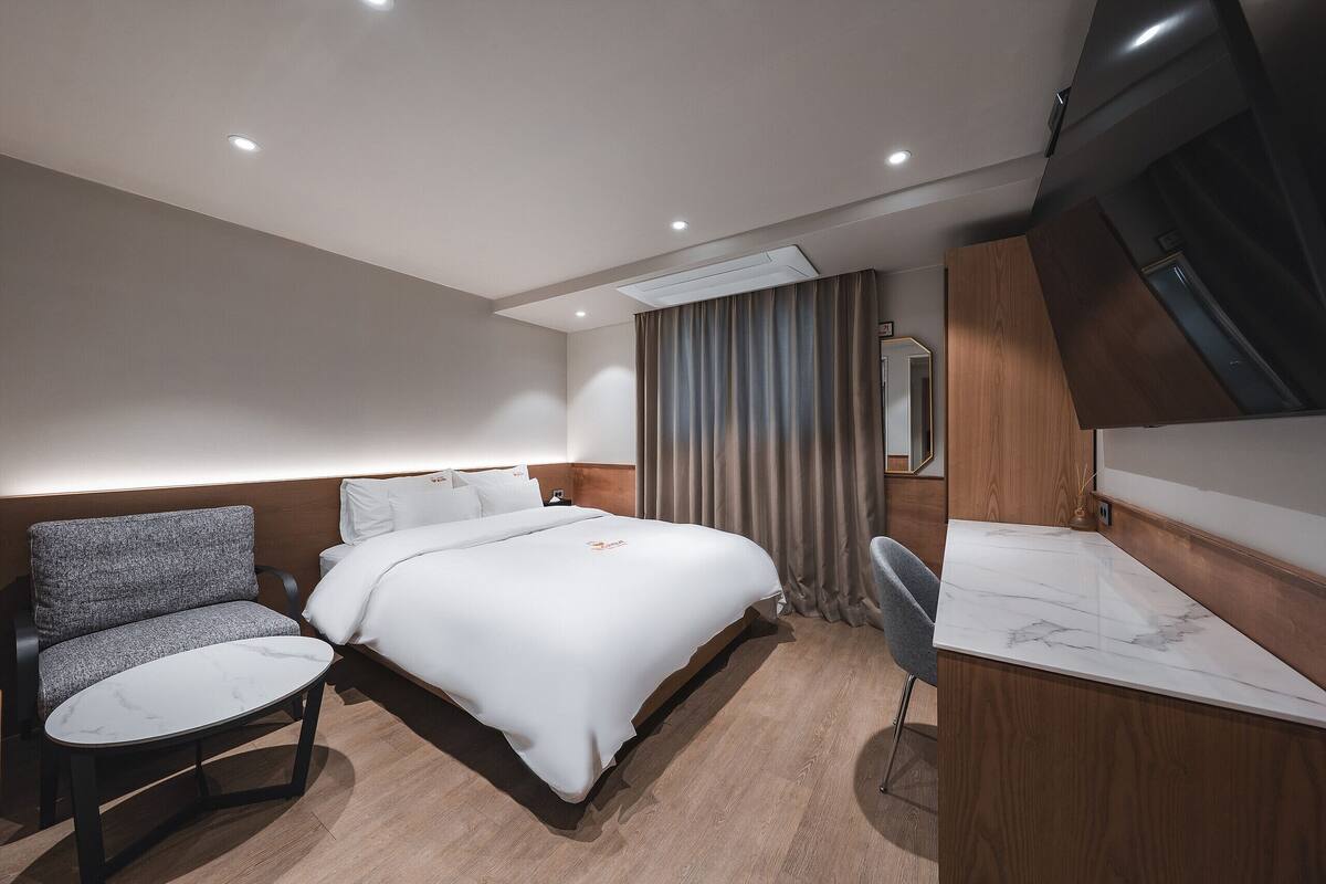 A modern hotel room with a bed, a seating area, a desk, and a shower area.