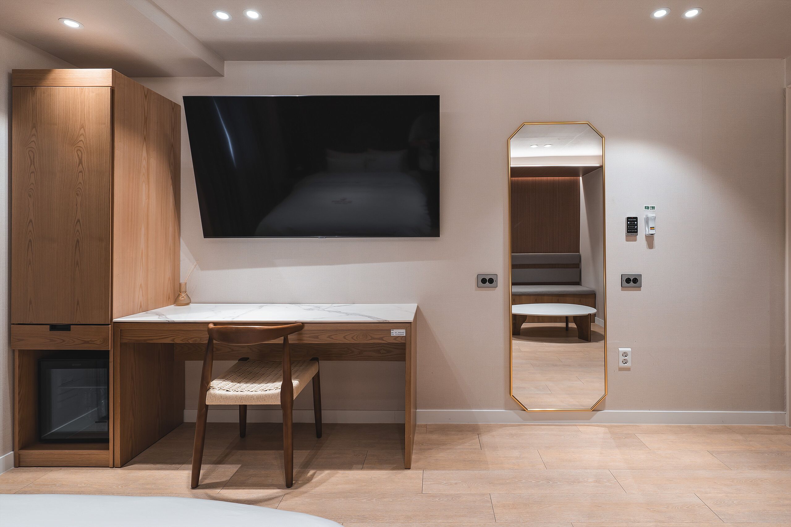 Une chambre moderne avec un bureau en bois, un grand téléviseur à écran plat, un miroir et une armoire intégrée.