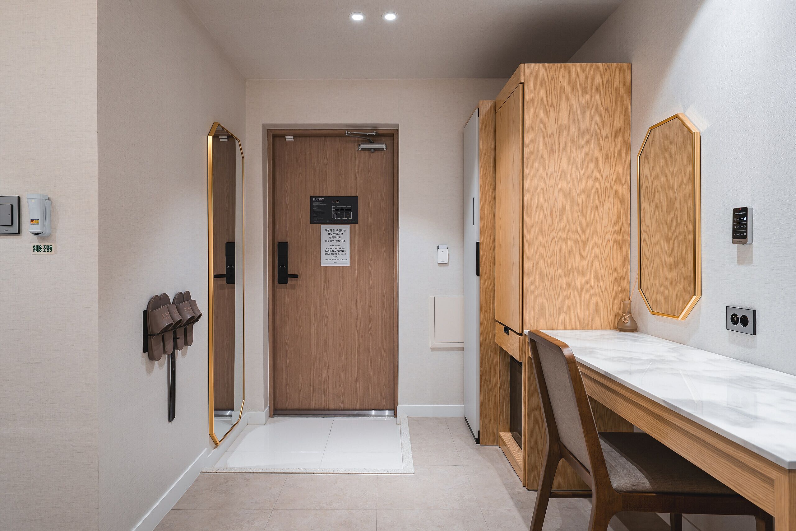 A hallway with a wooden door, a mirror, a desk, and a chair.