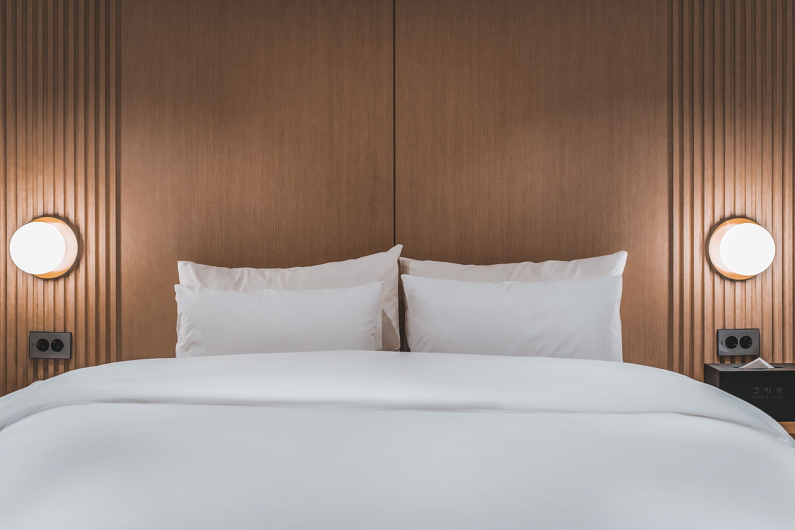A neatly made bed with white linens and two bedside lamps.