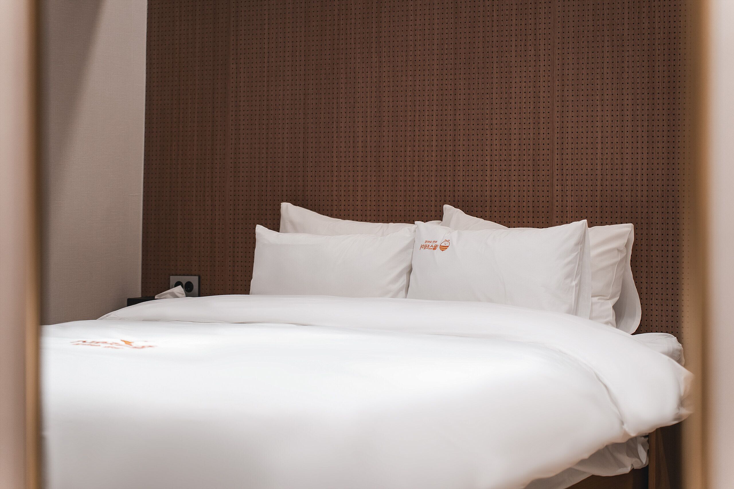 A neatly made bed with white linens and pillows, a wooden headboard, and a small bedside table with a lamp.