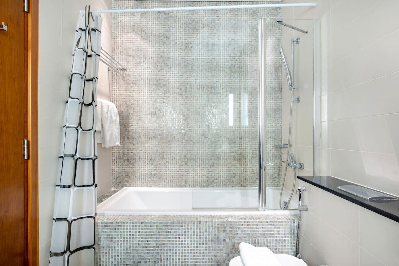 A modern bathroom with a glass-enclosed shower, a white bathtub, and mosaic tile walls.