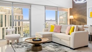 A modern living room with a sectional sofa, a coffee table, and a view of the city through large windows.