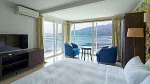 A hotel room with a large bed, a TV, a desk, two chairs, a lamp, and a view of the sea. - Hotel Himalaya Sea (Ito)