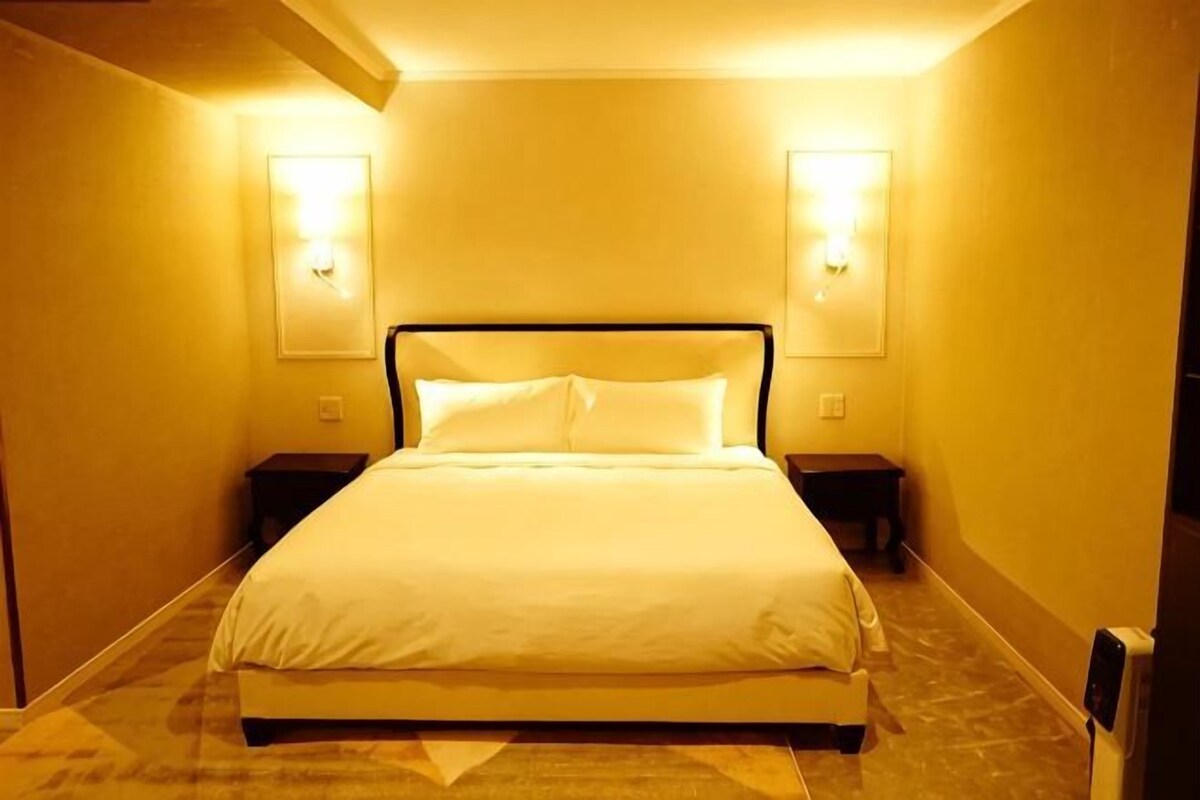 A hotel room with a large bed, two bedside tables, and wall-mounted lights.