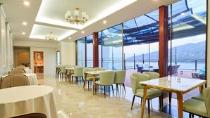 A modern dining area with tables and chairs, large windows with a view of the sea, and a chandelier. - Hotel Himalaya Sea (Ito)