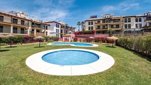 A residential area with two swimming pools, a well-maintained lawn, and multi-story buildings with balconies.