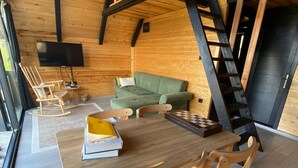 A cozy wooden cabin interior with a dining table, chairs, a green sofa, and a TV mounted on the wall. - Pileki Bungalov (Iyidere)