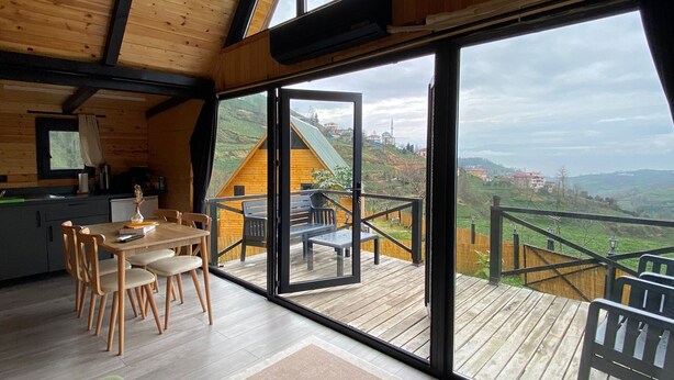 A spacious loft with a high ceiling, large windows, a wooden deck, and a dining area. - Pileki Bungalov (Iyidere)