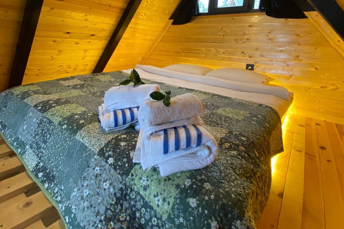 Une chambre confortable située sous les toits, avec un plafond en pente, un lit recouvert d’une literie à motifs floraux et un luminaire suspendu.