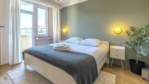 Une chambre à coucher avec un lit, des tables de chevet, une plante en pot et une vue par la fenêtre.